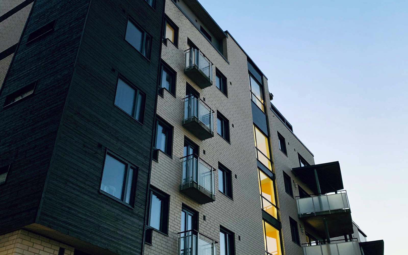 A multifamily building with brick, dark cladding, balconies, and large windows.